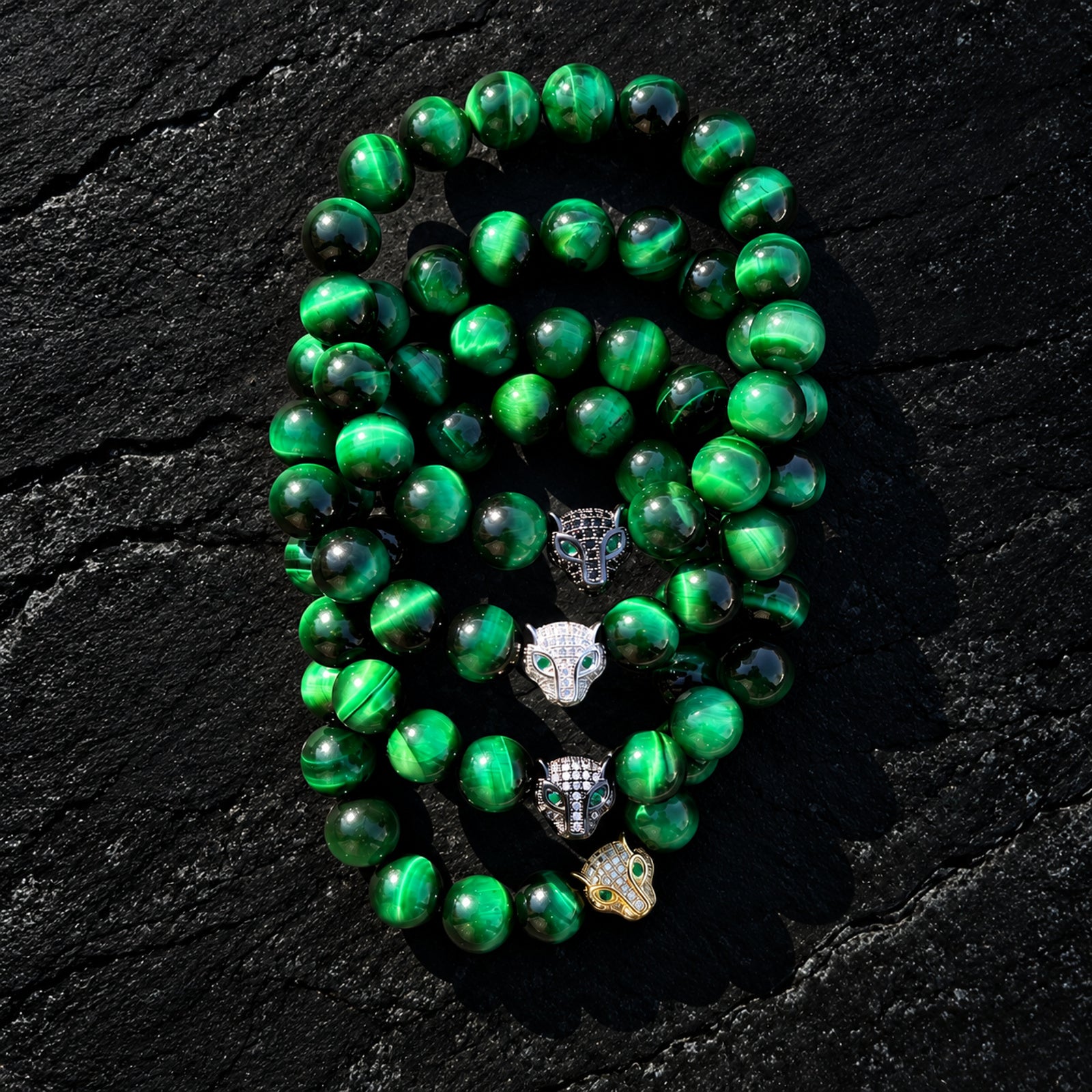 Four green tiger's eye bracelets with jaguar heads in contrasting metallic finishes and green eyes, arranged together.