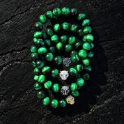 Four green tiger's eye bracelets with jaguar heads in contrasting metallic finishes and green eyes, arranged together.